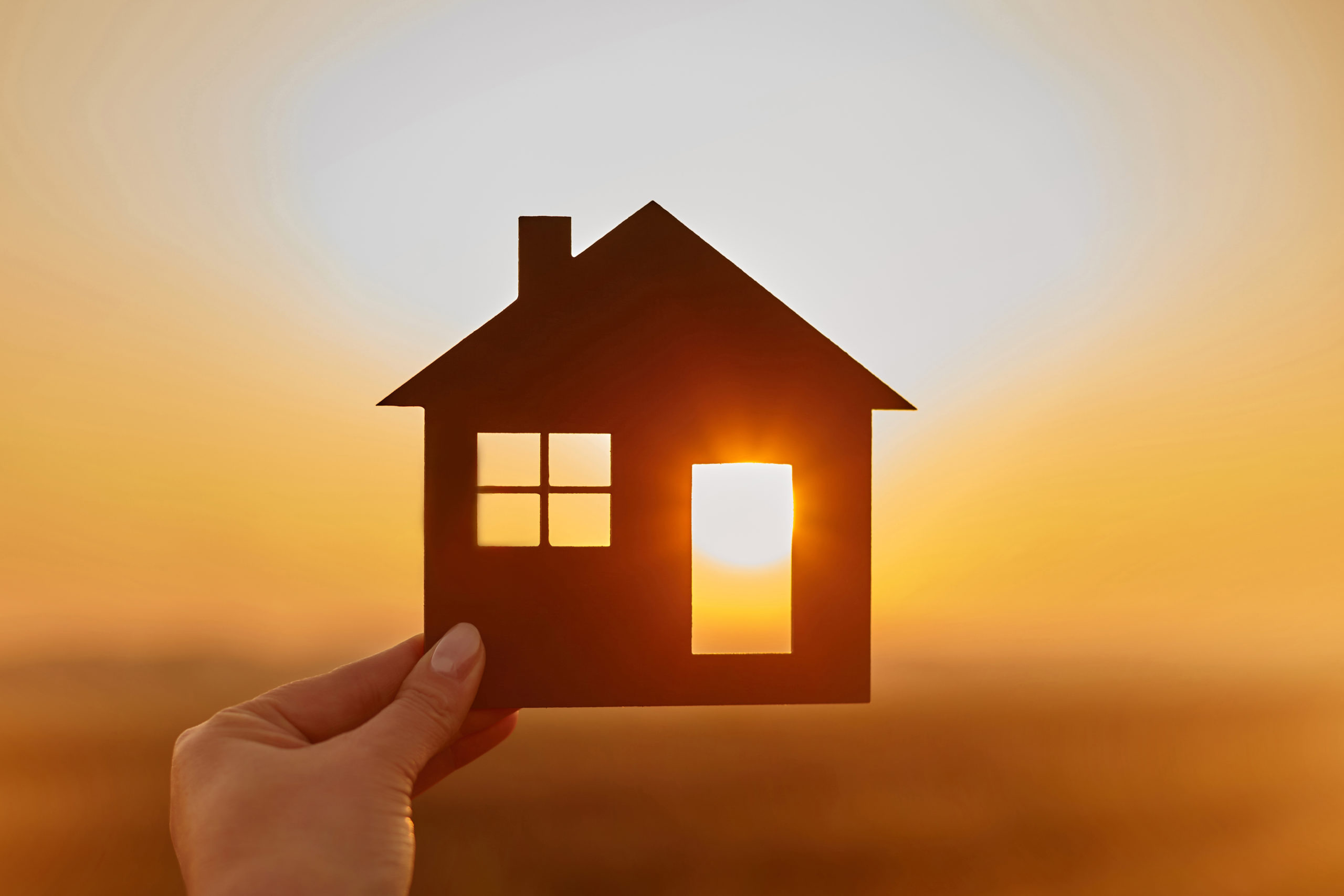 Woman hand holds wooden house against the sun